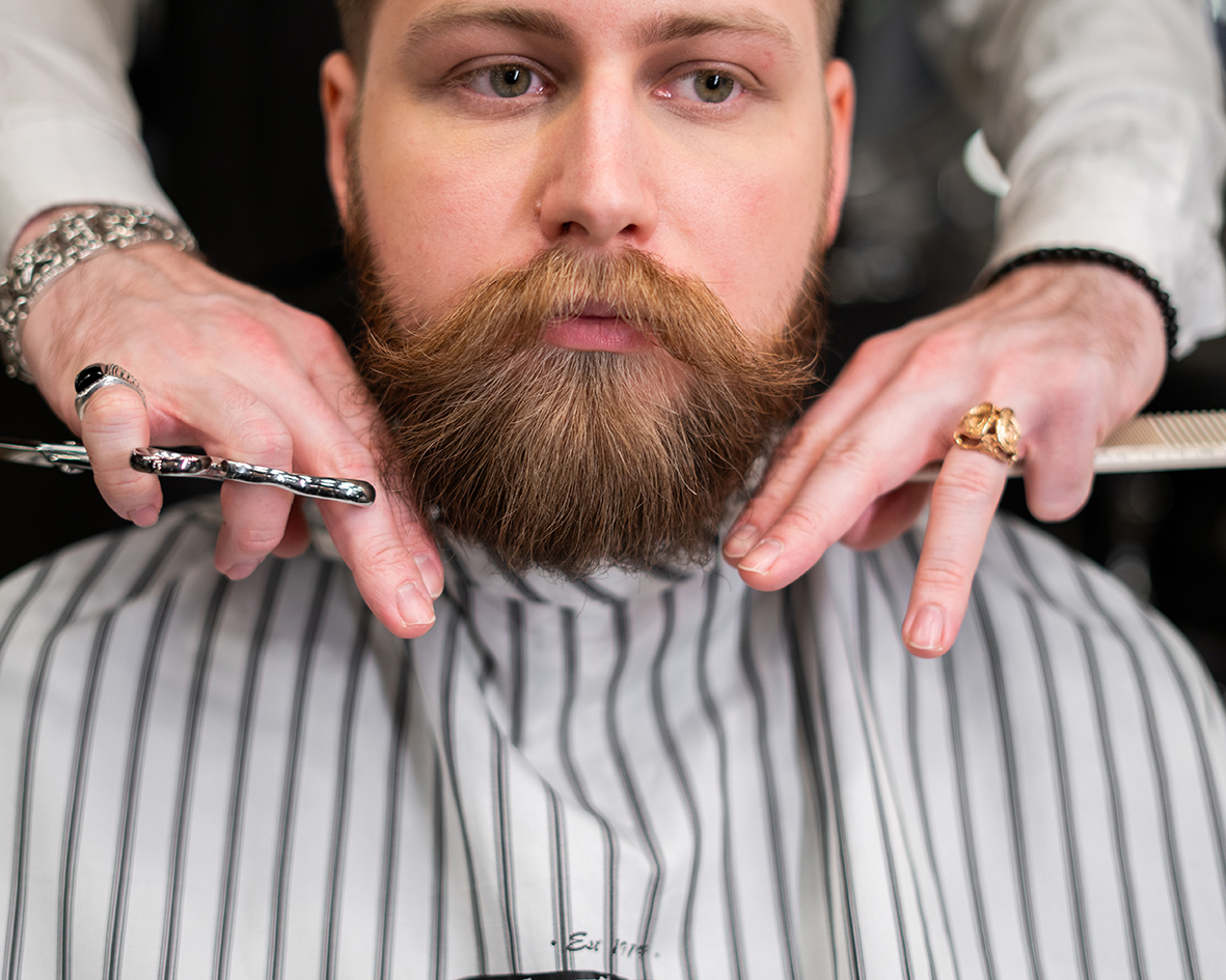 A client at the barber is having his beard groomed with the help of the beard balm.